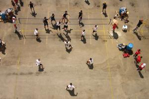 We look down from above at a  crowd of Asian-American men playing street volleyball.
