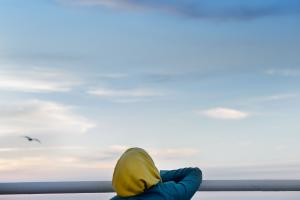 An individual in a yellow hijab sits in a chair in the stern of a boat before the ocean