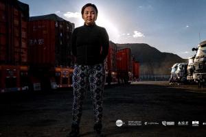 woman stands in front of trucks, mountains in the background