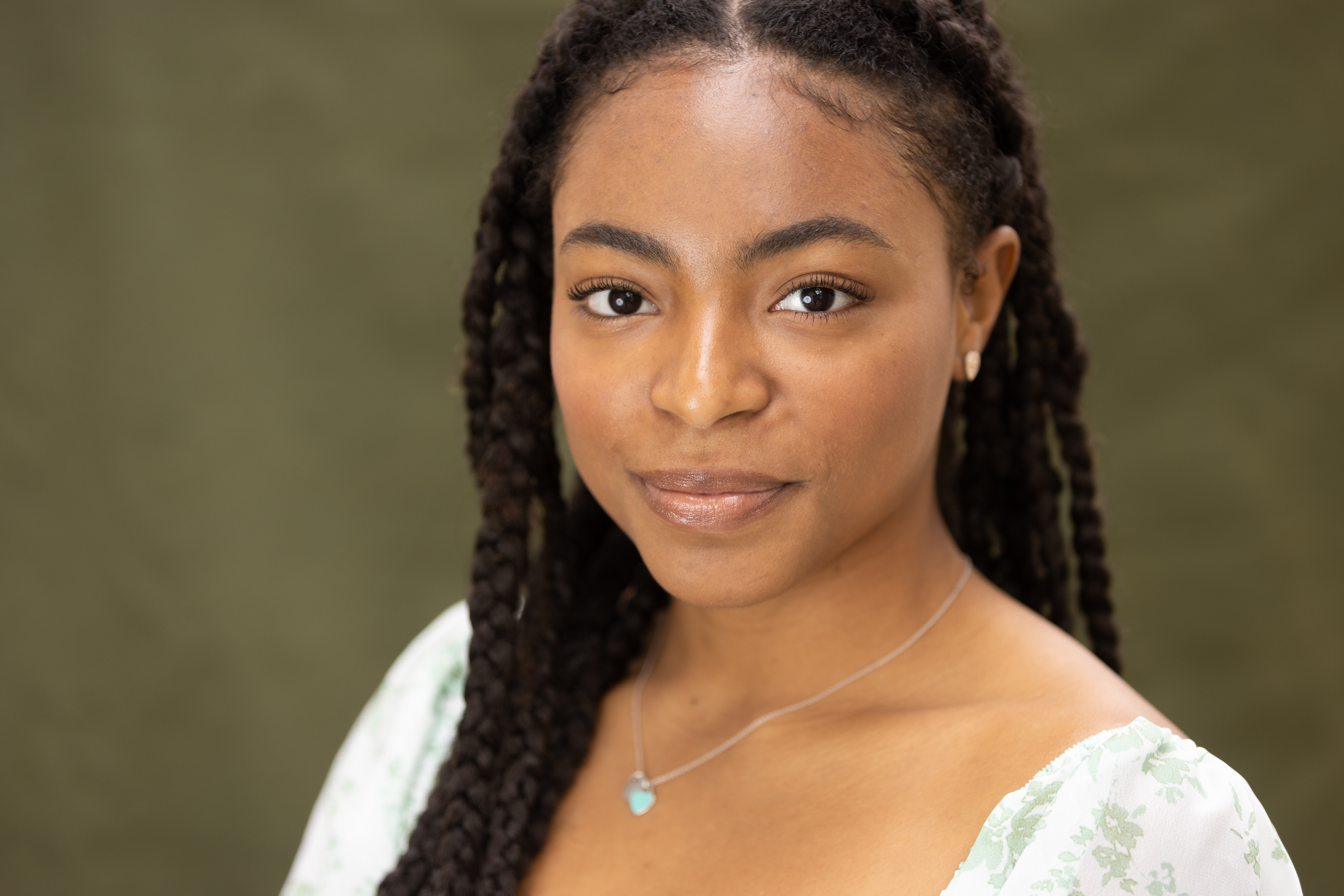 young adult with medium-light skin tone, braided hair, wearing blue heart necklace with a mint green shirt