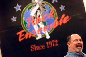 Doug Burris stands in front of 'Rock Ensemble' poster.