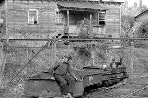 Early 20th century West Virginian miners sit on mine carts outside of a wooden house.