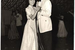 Mary and Kelly Adachi smile and slow dance in their wedding outfits. 