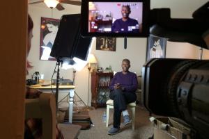 A queer black elder sits with their legs crossed during an interview in their mid-sized artistically decorated Living Room
