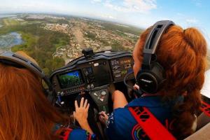 two red-headed women at the controls of an aircraft in midflight - green landscape stretches out beyond the clear glass cockpit window.