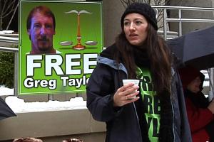 A woman stands in front of a 'Free Greg Taylor' poster.