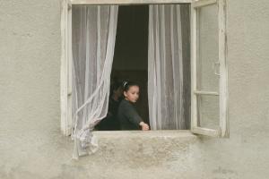 A young girl stares out the open window of a rustic stone building