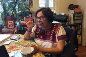 Photograph of Judy Heumann waving at the camera and smiling.