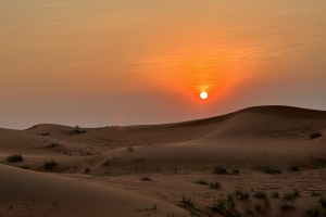 A serene desert landscape at sunset, with the sun casting a warm orange glow across the sky.