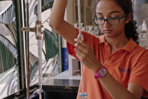 A student is in lab extracting a liquid using a syringe. 
