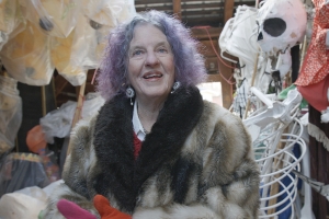 Halloween Parade director Jeanne Fleming, with purple hair and a flamboyant fur coat, stands in awe in the barn where she stores fifty years of puppets.