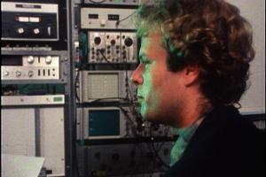 Ken Kelley stares in profile, surrounded by towers of sound recording equipment. 