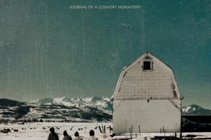 four monks walk outside of a white monastery covered in snow. Mountains break the horizon in the distance.