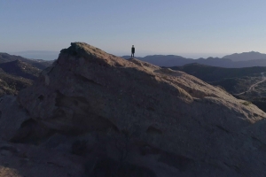 Blue skies and mountains with a person standing alone on one mountain.