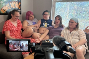 Five individuals sit on a couch in front of a camera