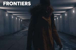 An unidentifiable man stands in a dark hallway underground.