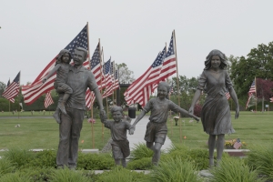 Still from 'Richland' depicting a statue of a family walking proudly in front of two columns of American flags, which border a series of manicured lawns. Photo credit: Helki Frantzen