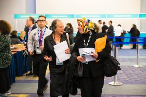Two women are talking while walking away from a booth in a conference.