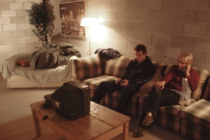 A lo-fi image of two young people sitting on a plaid couch, looking at a small TV.