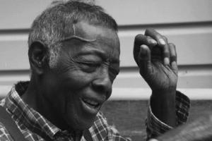 A black & white image of an elderly man of African-American descent sitting on a porch.