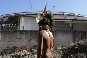 A Brazilian in traditional clothing looks at the soccer stadium outside.
