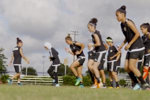 female football team runs laps on a green field in black uniforms