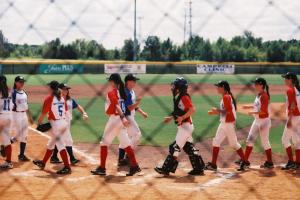 opposing female baseball teams high five in the baseball field at the end of the game.