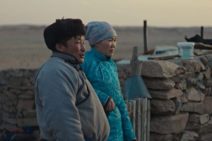 Two people dressed in traditional Mongolian clothes look into the distance.