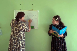 Film still from 'Writing Hawa' featuring two women - one with a book in hand, the other writing on a whiteboard.