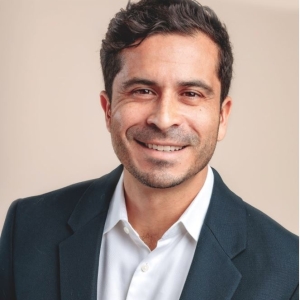 Headshot of a middle-aged male of Spanish descent in a navy blue blazer. 