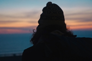 Film still from 'Your Friend Memphis': the silhouette of a person's back, as they look out to a sunset over the ocean.