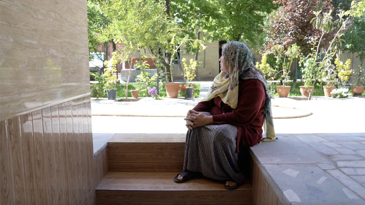 A woman sitting on steps looking out into a courtyard.