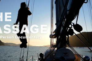 Jessie hangs from the ropes of her sailboat, peering into the sunset over the horizon.