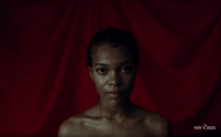 A Black woman with short curly hair stands in front of a red background, bare-shouldered and staring at the camera. From Juliana Kasumu’s Baby Bangz: Black Power in Hair.