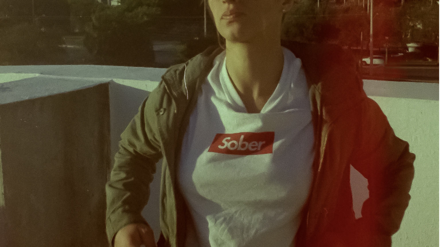 Screenshot from 'Shuffle' via sxsw.com. A person wearing a white shite with red and white logo that reads "Sober" under a green jacket.