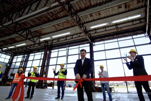 An AI-generated video of a factory floor with glass walls and a man in a black suit holding a floating red ribbon.