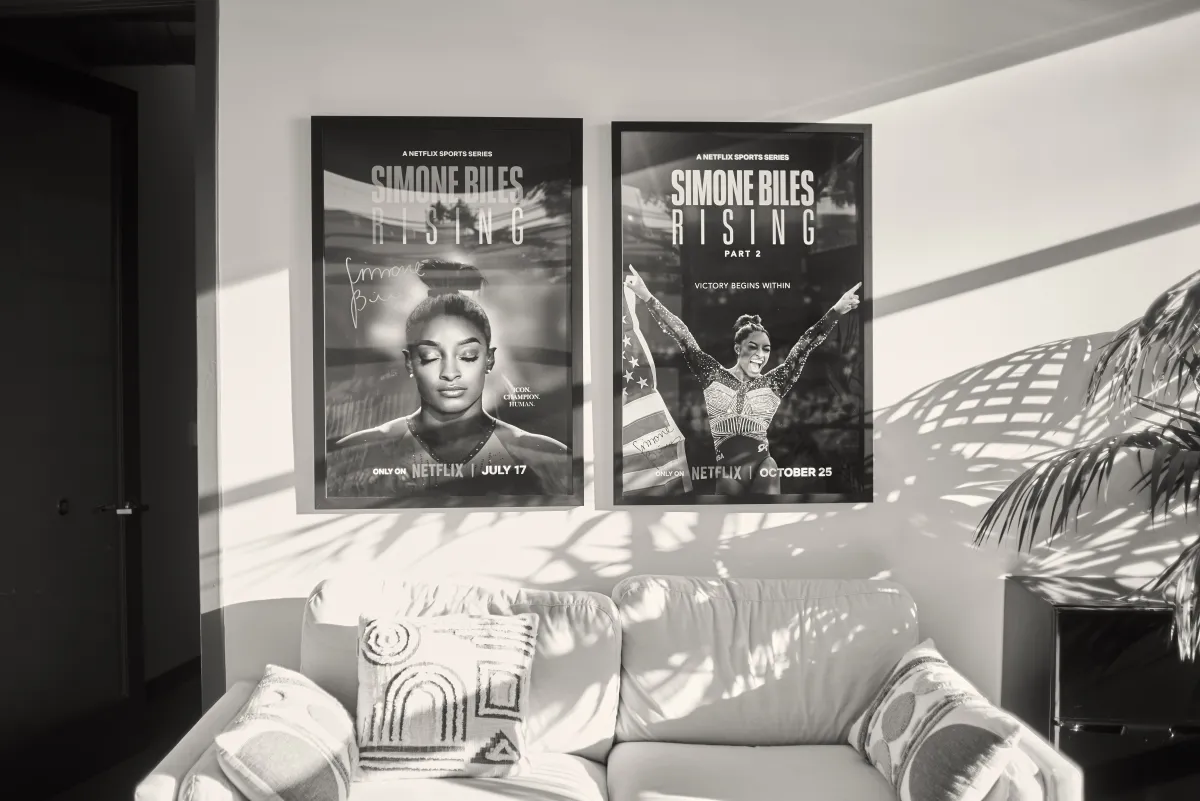 Black and white photograph of Simone Biles Rising posters above a white coach in a sunny office.