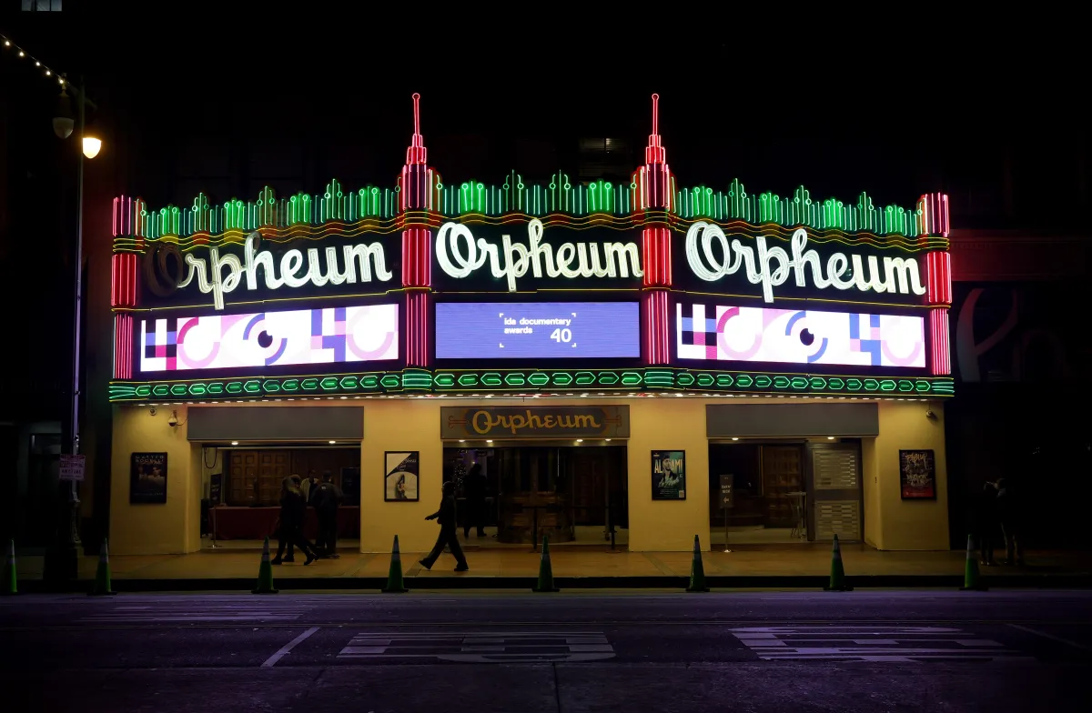 Photo of the outside of a theater, with a lit up marquee of the 40th IDA Documentary Awards' pink and purple graphics.