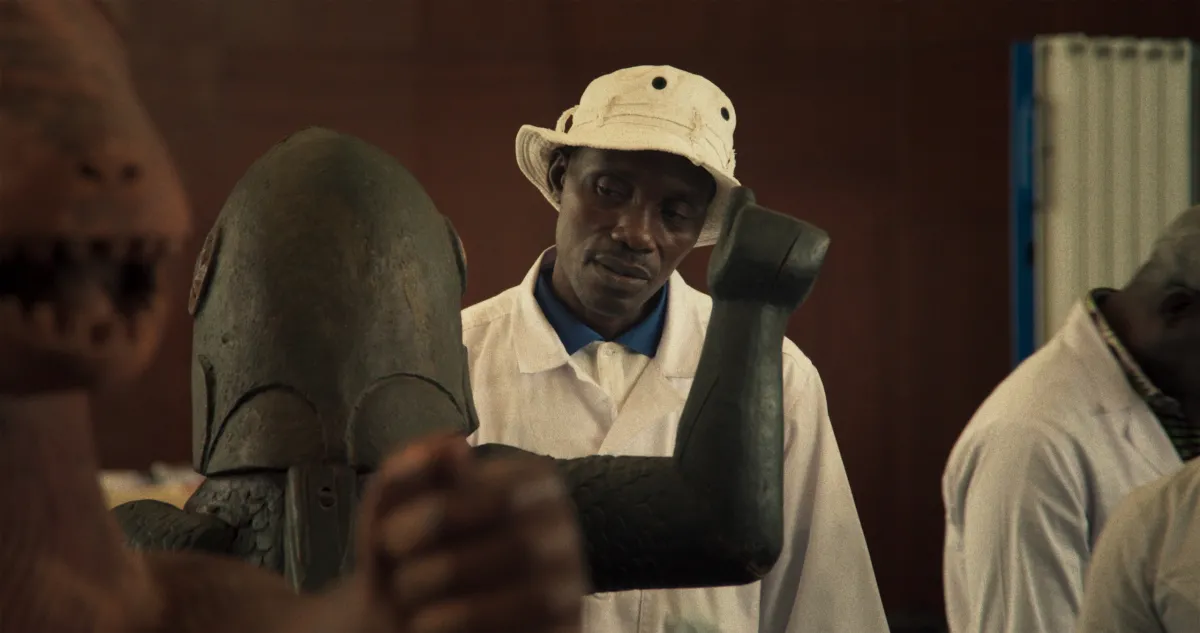 Black man in white bucket hat looks over an artifact.