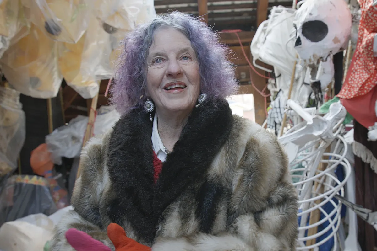 Halloween Parade director Jeanne Fleming, with purple hair and a flamboyant fur coat, stands in awe in the barn where she stores fifty years of puppets.