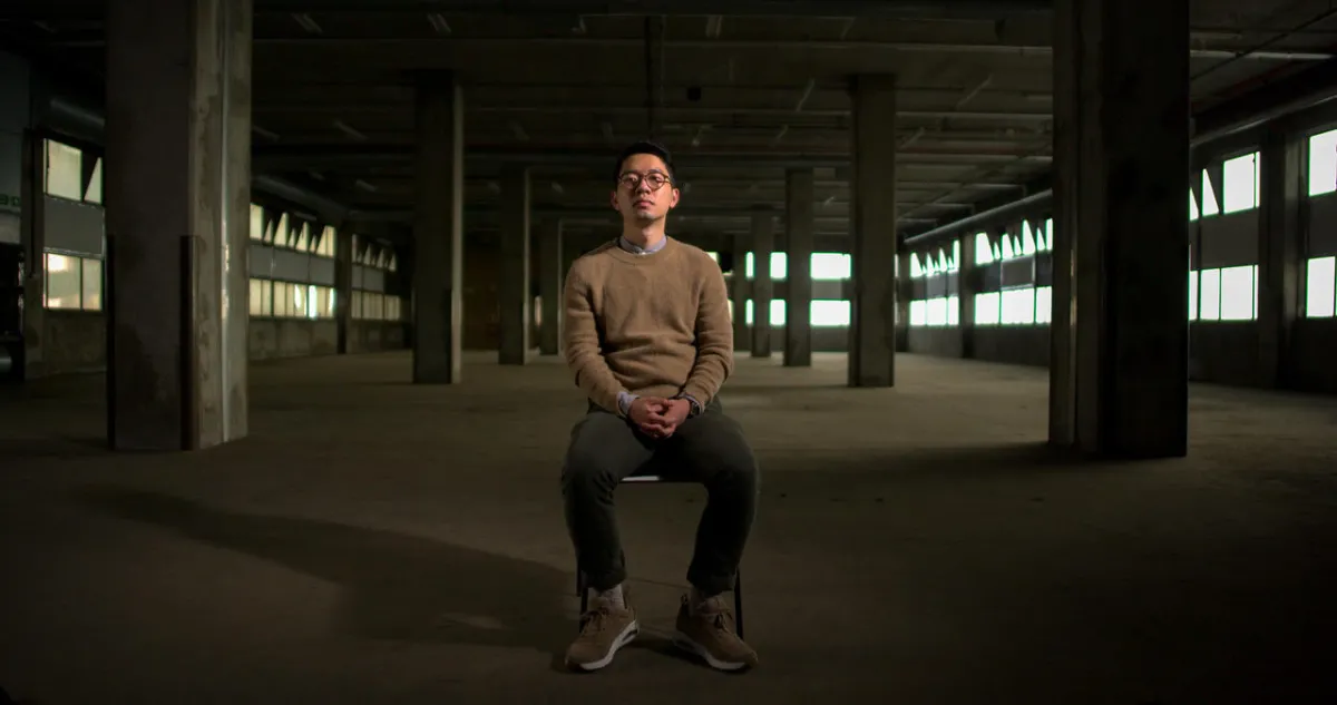 an asian man sits in the middle of an abandoned warehouse