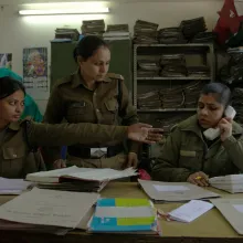 Three female police officers in uniform in a crowded office.