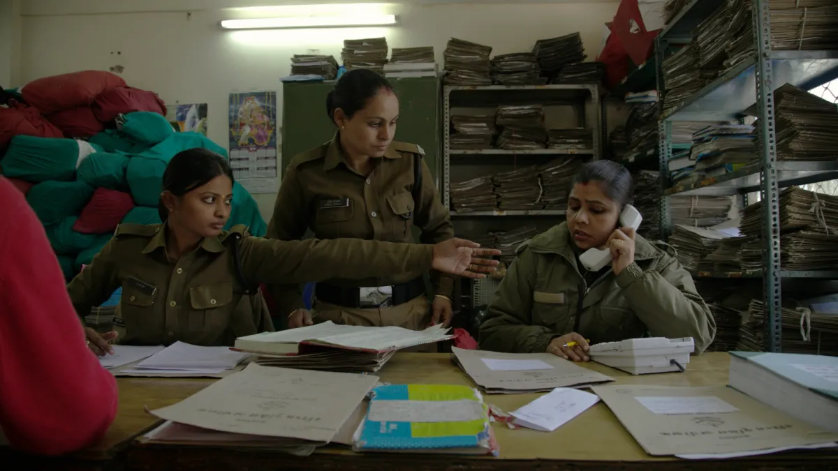 Three female police officers in uniform in a crowded office.