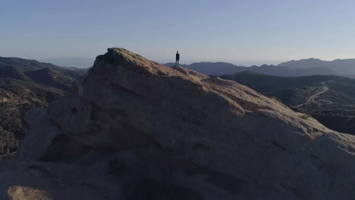Blue skies and mountains with a person standing alone on one mountain.