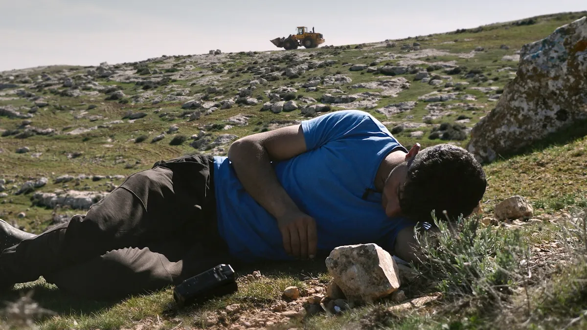 man reclines on a rock hill with a tank in the background