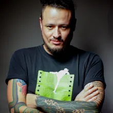 Headshot Rodolfo Castillo Morales with arm tattoos and a black t-shirt with a green and white print