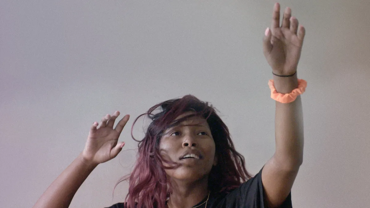 A young woman practices the movement of falling - her eyes gaze upward and hands are up in the air.