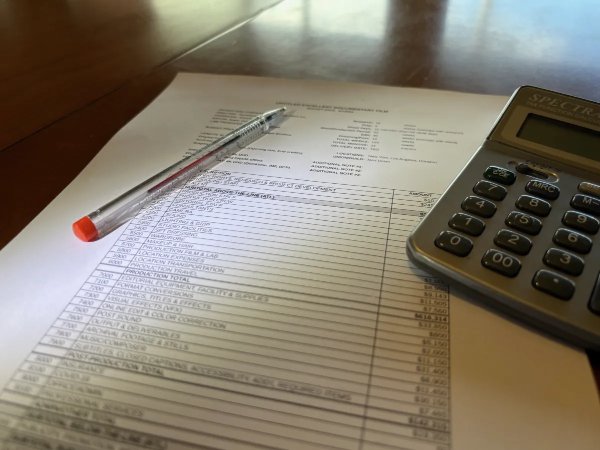 Photograph of a print out of a budget topsheet, a pen, and a calculator.