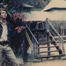 A merged image of two photographs of a young white man in front of Southeast Asia looking buildings.