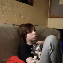 On a beige couch, a teenaged boy sits with his cat.